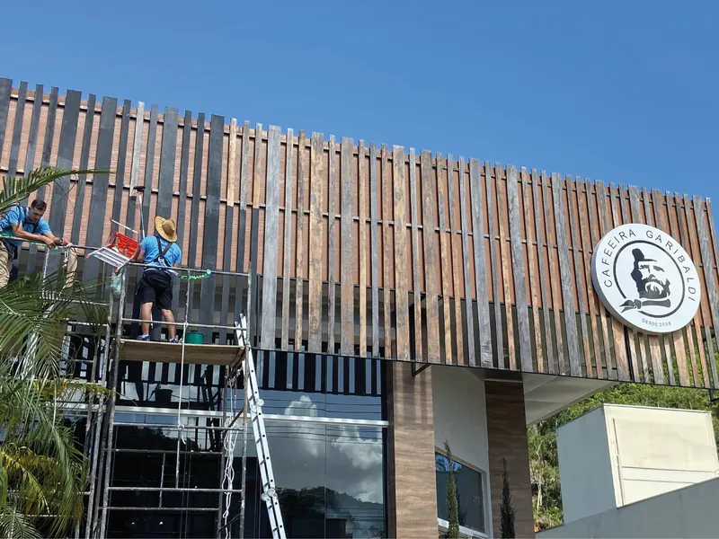 Equipe da FR Soluções sobre andaime pintando o brise de madeira da fachada da Cafeeira Garibaldi