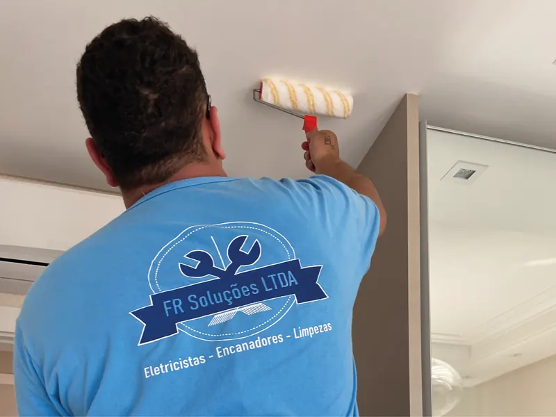 Pintor da FR Soluções aplicando tinta com rolo no teto, junto ao canto da parede